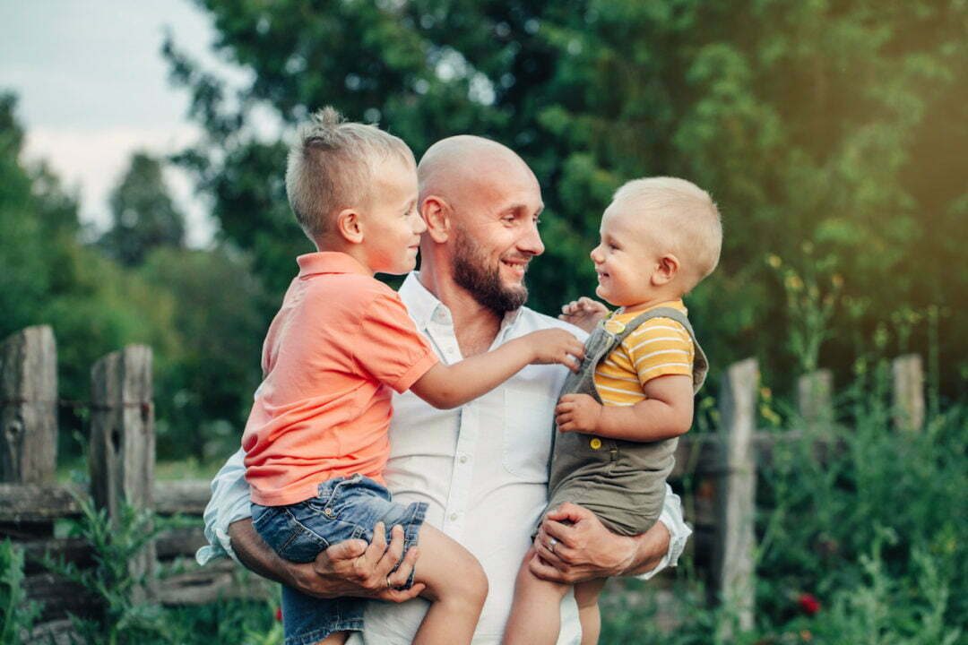 Photo d'un homme portant 2 enfants : un garçon dans chaque bras